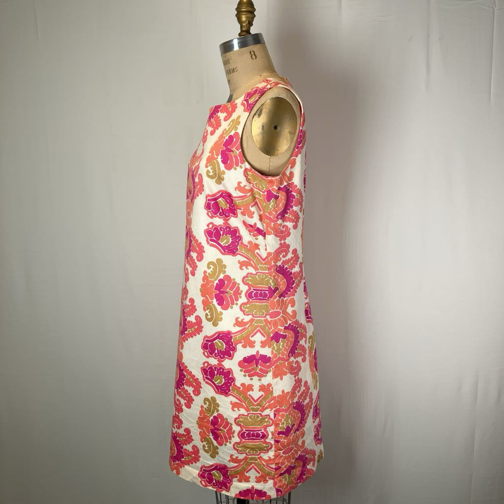 A sleeveless shift dress with a vibrant pink, orange, and green floral pattern on a cream background, displayed on a vintage dress form mannequin against a neutral light gray backdrop.