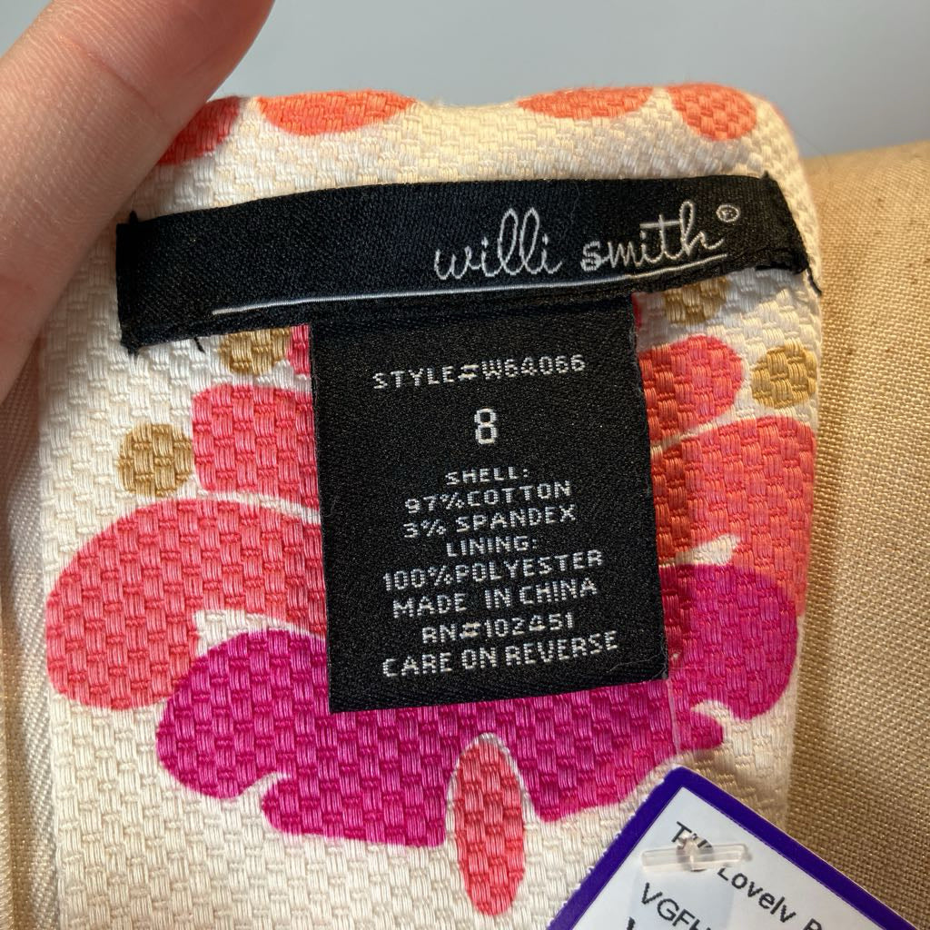 Close-up of a Willi Smith garment label sewn onto a floral fabric, with a finger holding the fabric. The label shows size 8 and material details: shell 97% cotton, 3/4 spandex lining, 100% polyester lining, made in China.