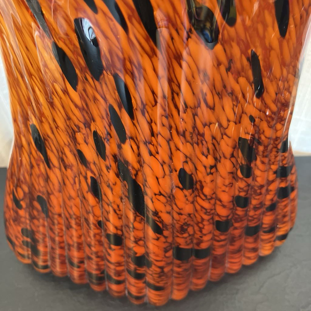 Close-up of a fluted glass vase with a vibrant orange and black marbled pattern, resting on a dark gray surface.