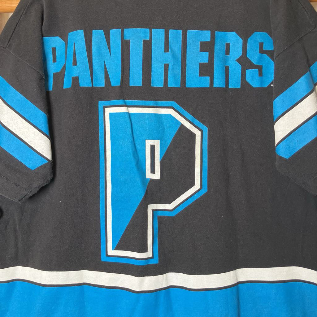 Close-up of the back of a dark charcoal gray jersey with bright blue and white lettering reading 'PANTHERS' and a large outlined letter 'P' on the back.