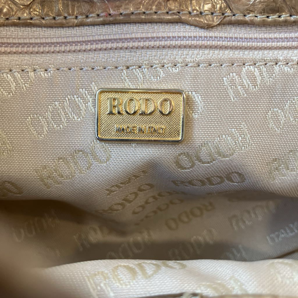 Close-up of the interior of a RODO bag, showing a gold-tone metal brand plaque on a beige monogrammed nylon lining.