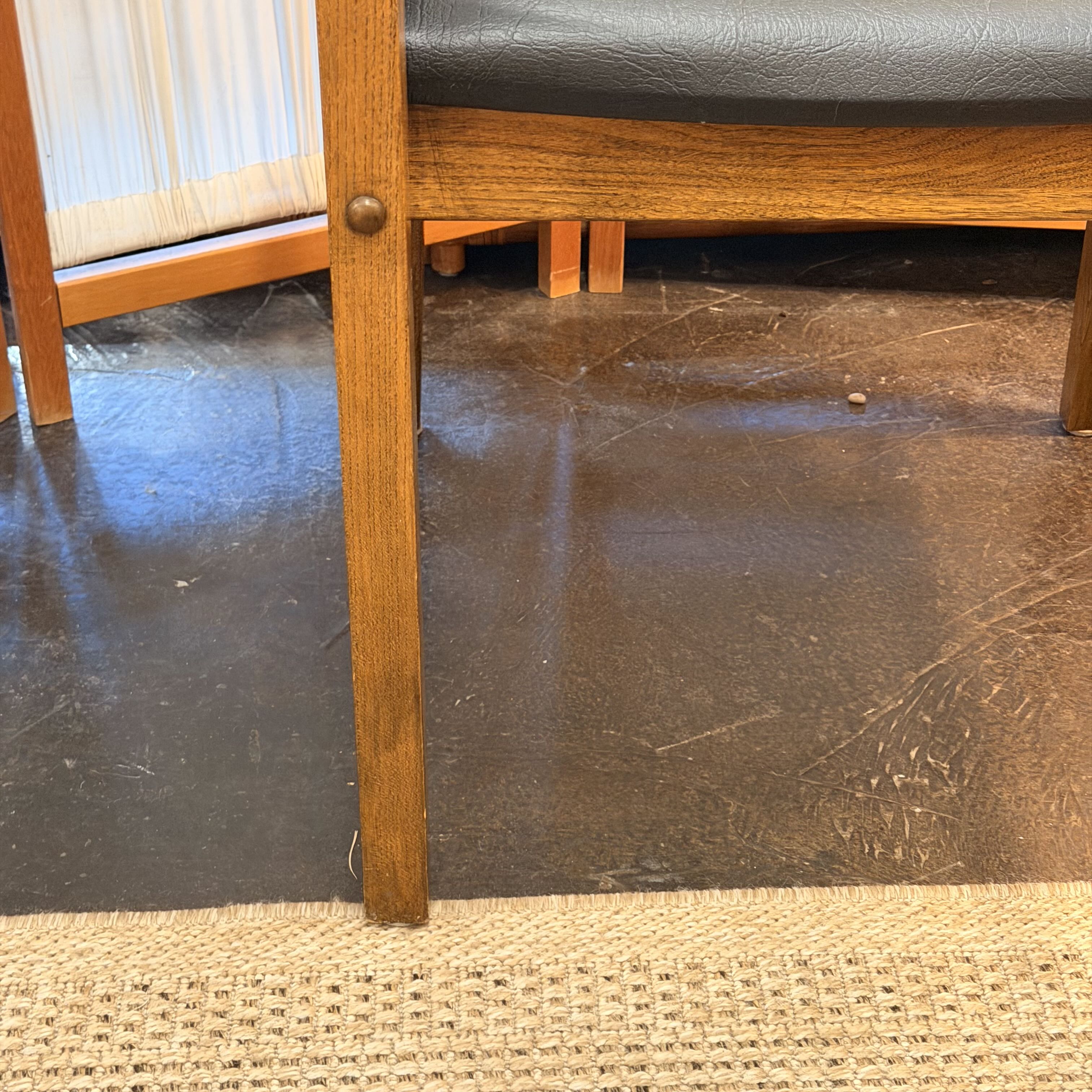 Close-up of a wooden chair leg with a dark upholstered seat, standing on a dark floor over a woven beige rug.