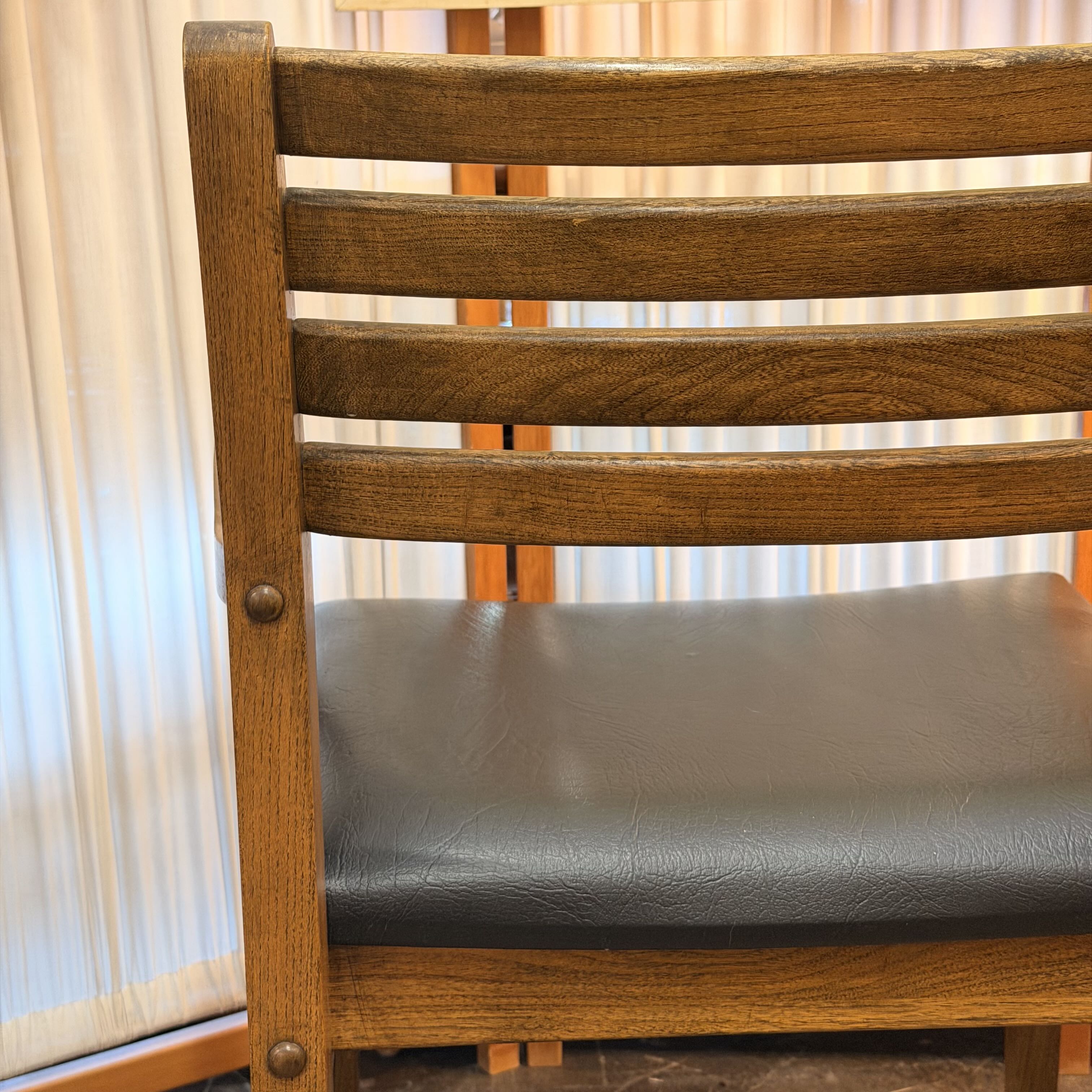 Close-up of a wooden chair with a slatted backrest and a dark gray upholstered seat cushion, photographed indoors against a light curtain background.