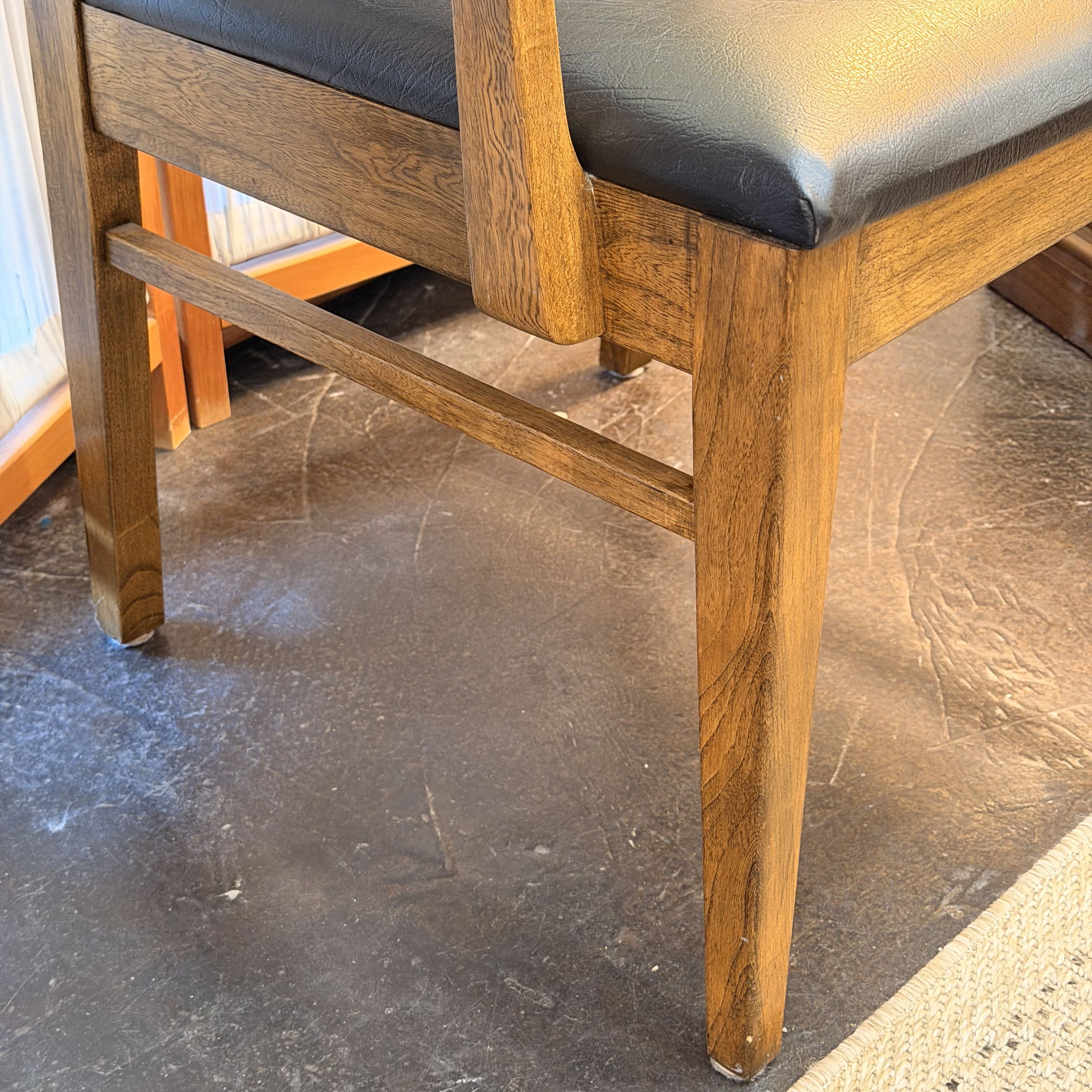 Close-up of a wooden dining chair with a black upholstered seat cushion, shown indoors on a dark floor.