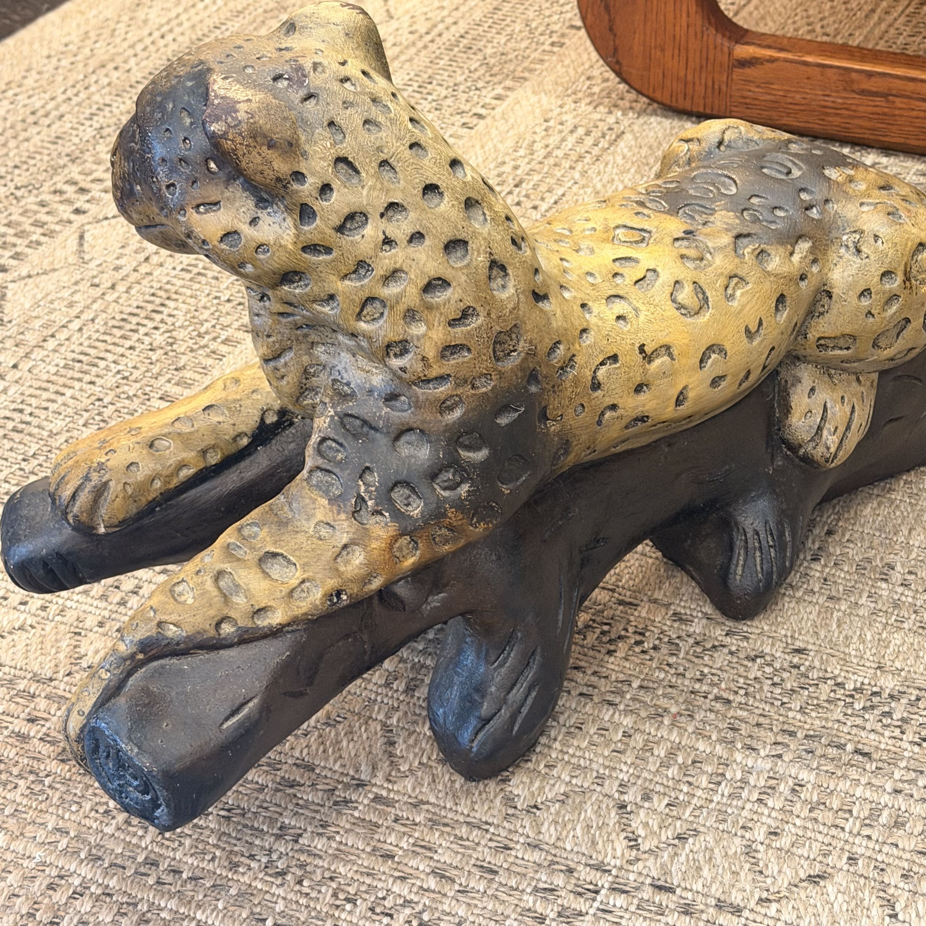 A decorative leopard figurine with a textured yellow and black spotted pattern, resting on a dark brown base against a woven beige fabric background.