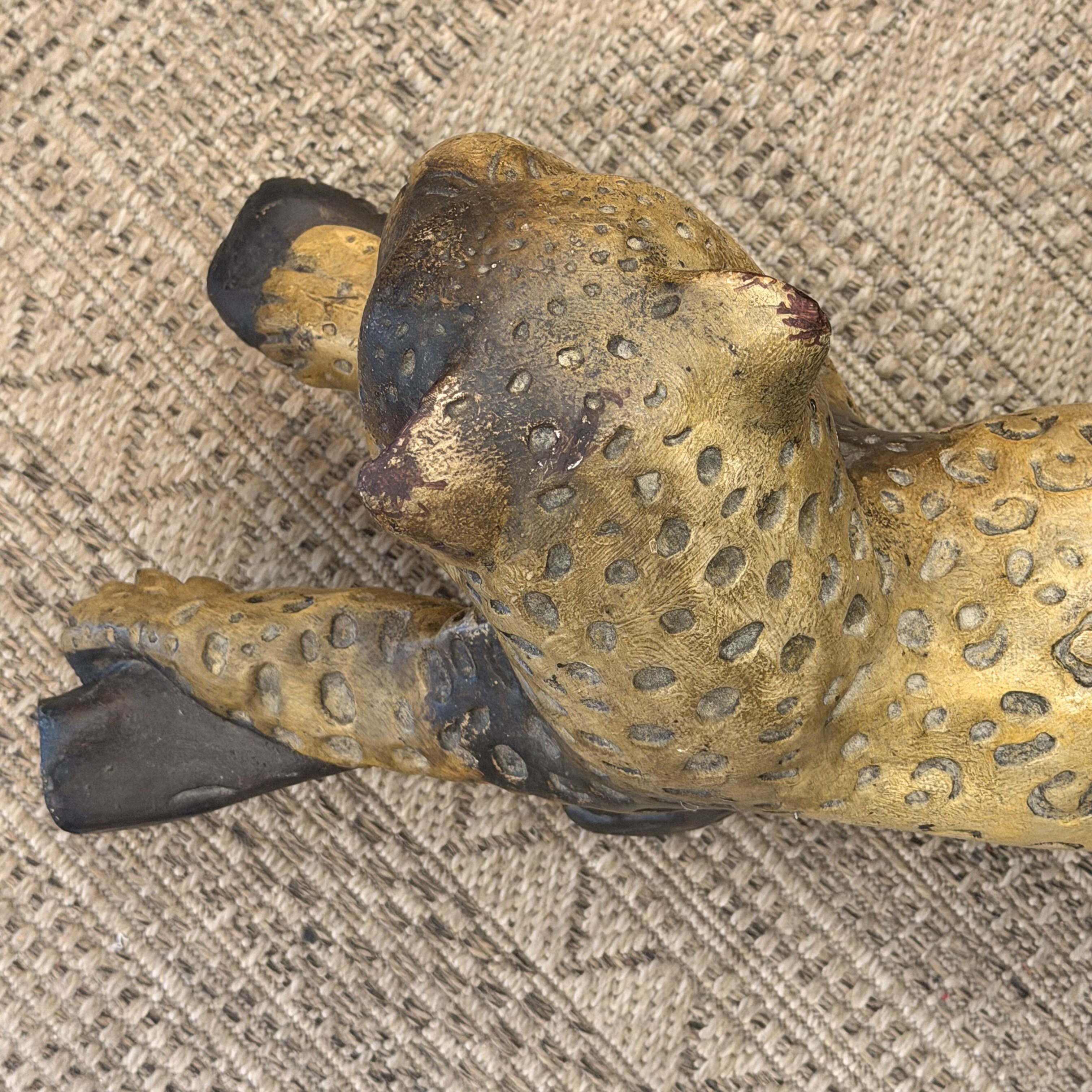 A close-up of a leopard figurine with a textured golden-yellow and black spotted pattern, lying on a woven beige fabric background.