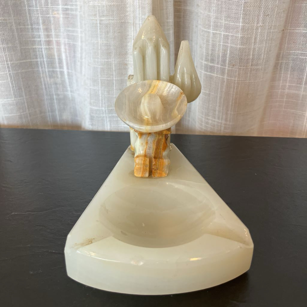 White alabaster carved ashtray on a dark surface and sheer curtain backdrop. 