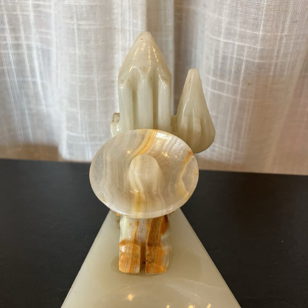 A polished onyx crystal cluster sculpture with multiple pointed and rounded crystal formations, displayed on a dark surface in front of a sheer curtain backdrop.