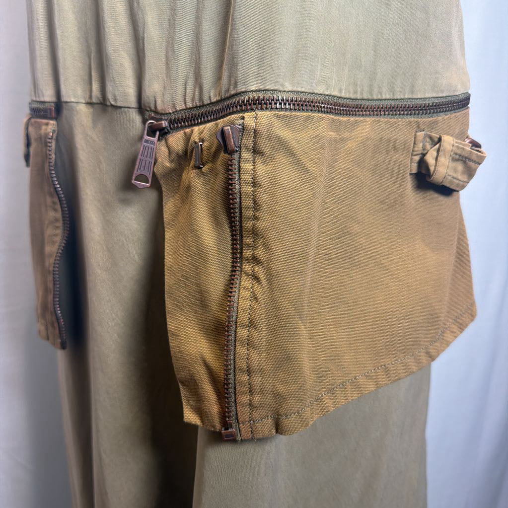 Close-up of a tan canvas utility pouch with multiple zippers attached to a beige garment, shown against a light gray background.