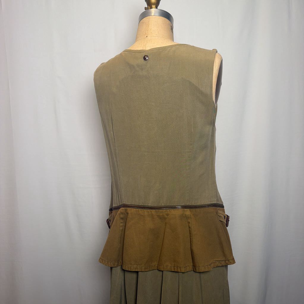 A sleeveless olive green top displayed on a dress form from the back, featuring a buttoned neckline, a brown waistband, and a pleated ruffle hem, paired with matching pleated skirt panels.