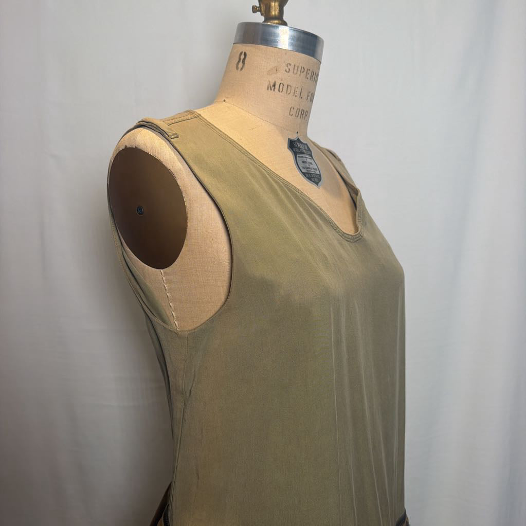 An olive green sleeveless top displayed on a vintage wooden dress form mannequin against a white fabric backdrop.