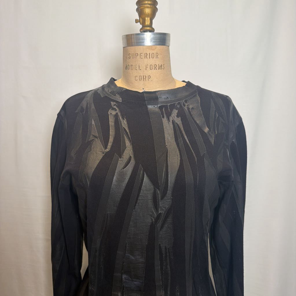 A black long-sleeve top with a textured, vertically striped abstract pattern, displayed on a vintage wooden model dress form against a white fabric backdrop.