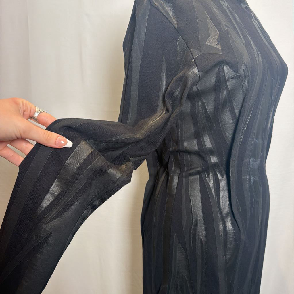 A close-up of a black sheer striped garment being held by a hand, showing its lightweight, semi-transparent fabric texture against a light neutral background.