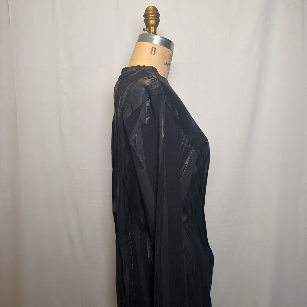 A black sheer long-sleeve top displayed on a dress form mannequin against a white fabric backdrop.