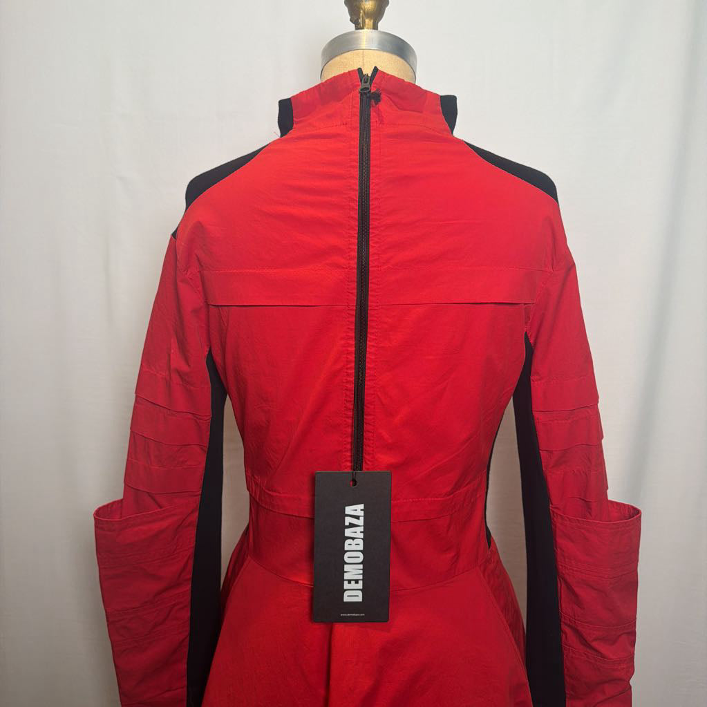A red and black Demobaza jacket displayed on a dress form mannequin, showing the back view with a black zipper and a black brand tag.