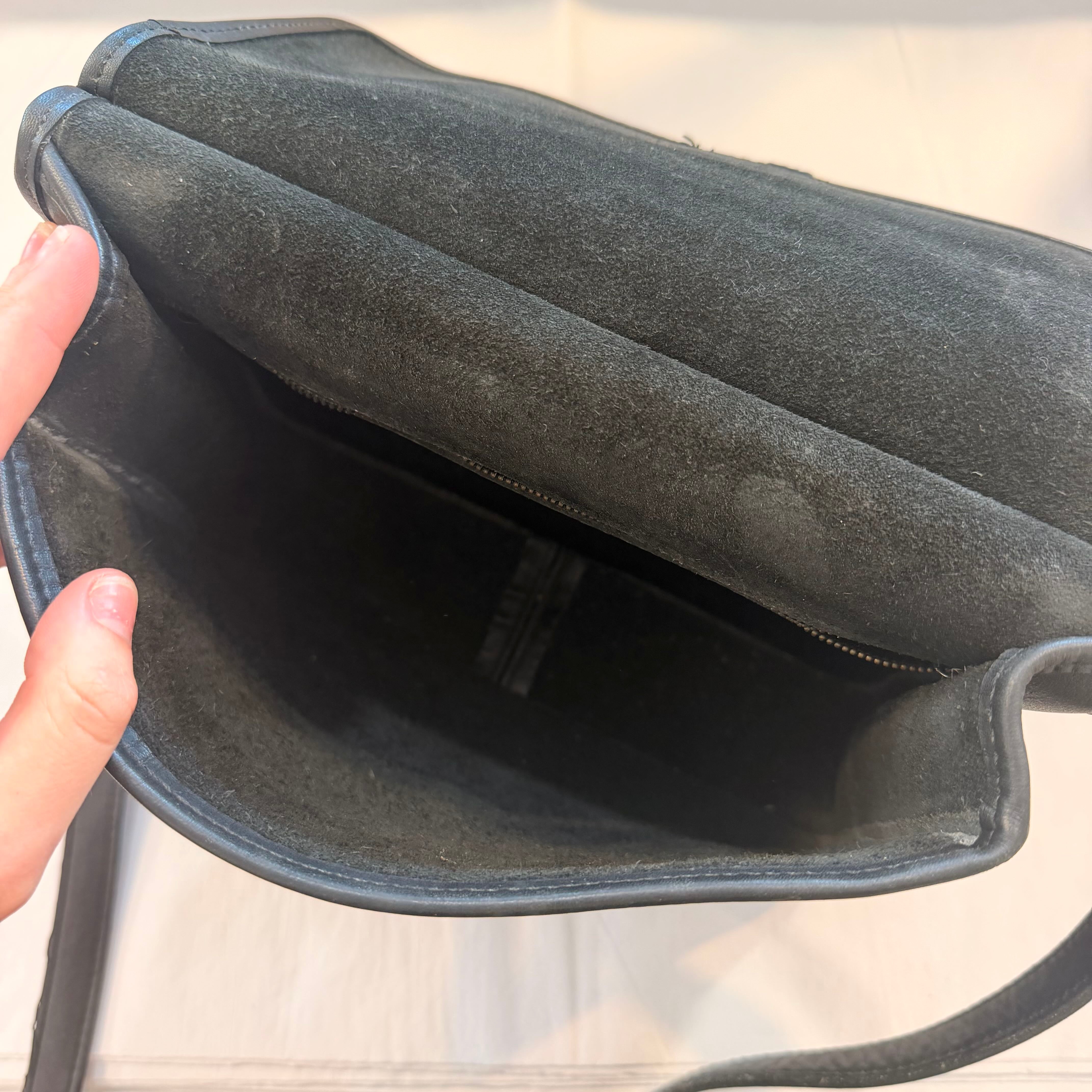 Close-up of a dark gray suede or faux-suede handbag interior being held open by a hand, showing the lining and zipper closure.
