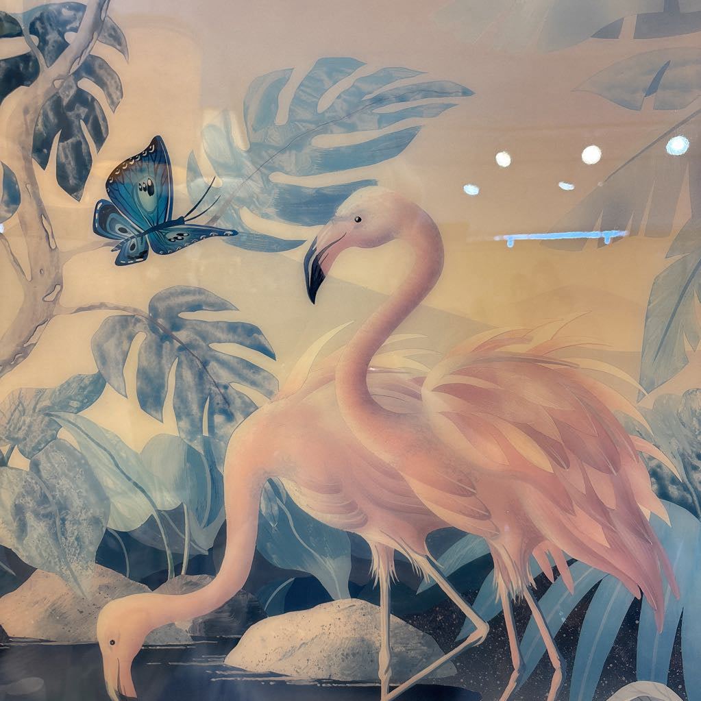 A decorative wall mural or wallpaper featuring a pink flamingo standing among blue tropical leaves, with a blue butterfly and soft beige background.