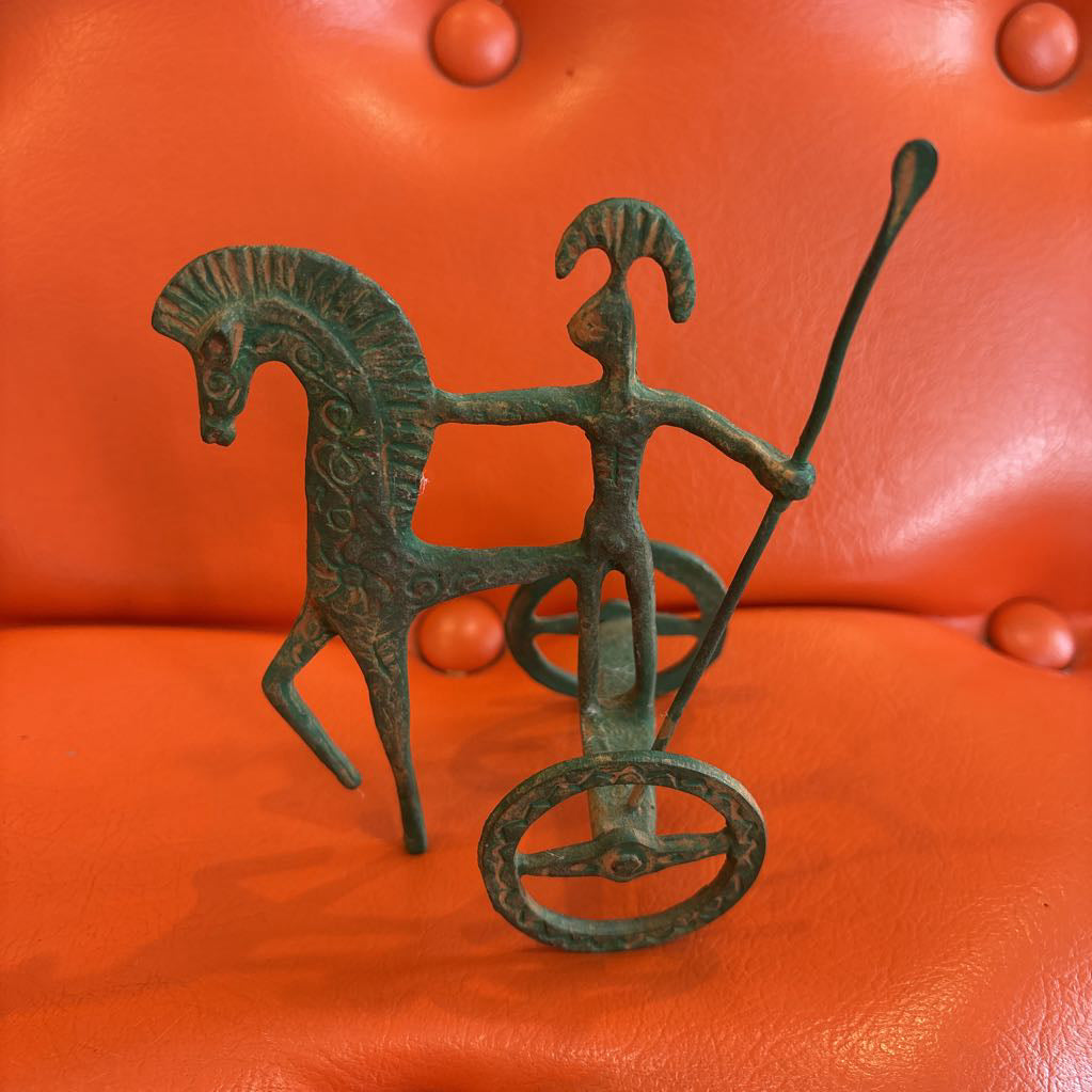 A metal ancient Greek style figure on an orange leather surface.