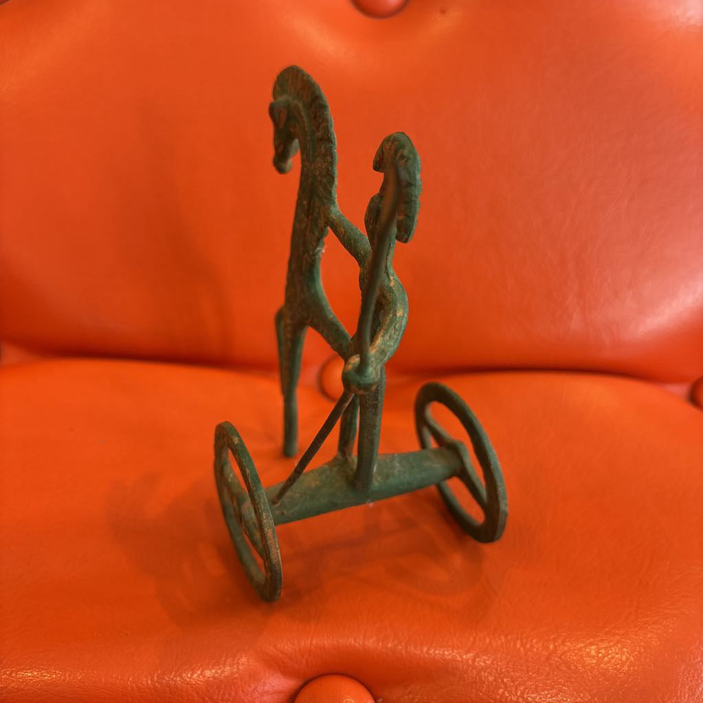 A metal ancient Greek style figure on an orange leather surface.