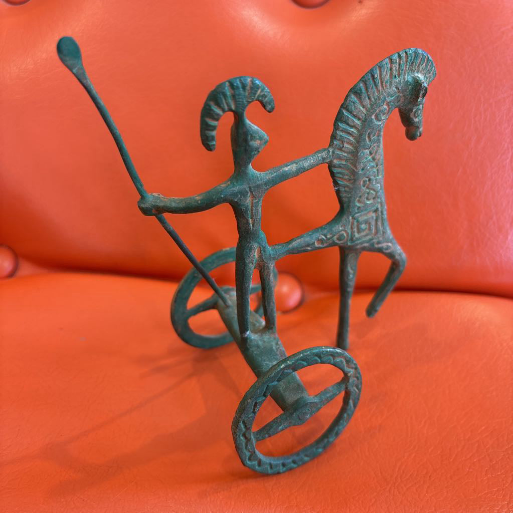 A metal ancient Greek style figure on an orange leather surface.