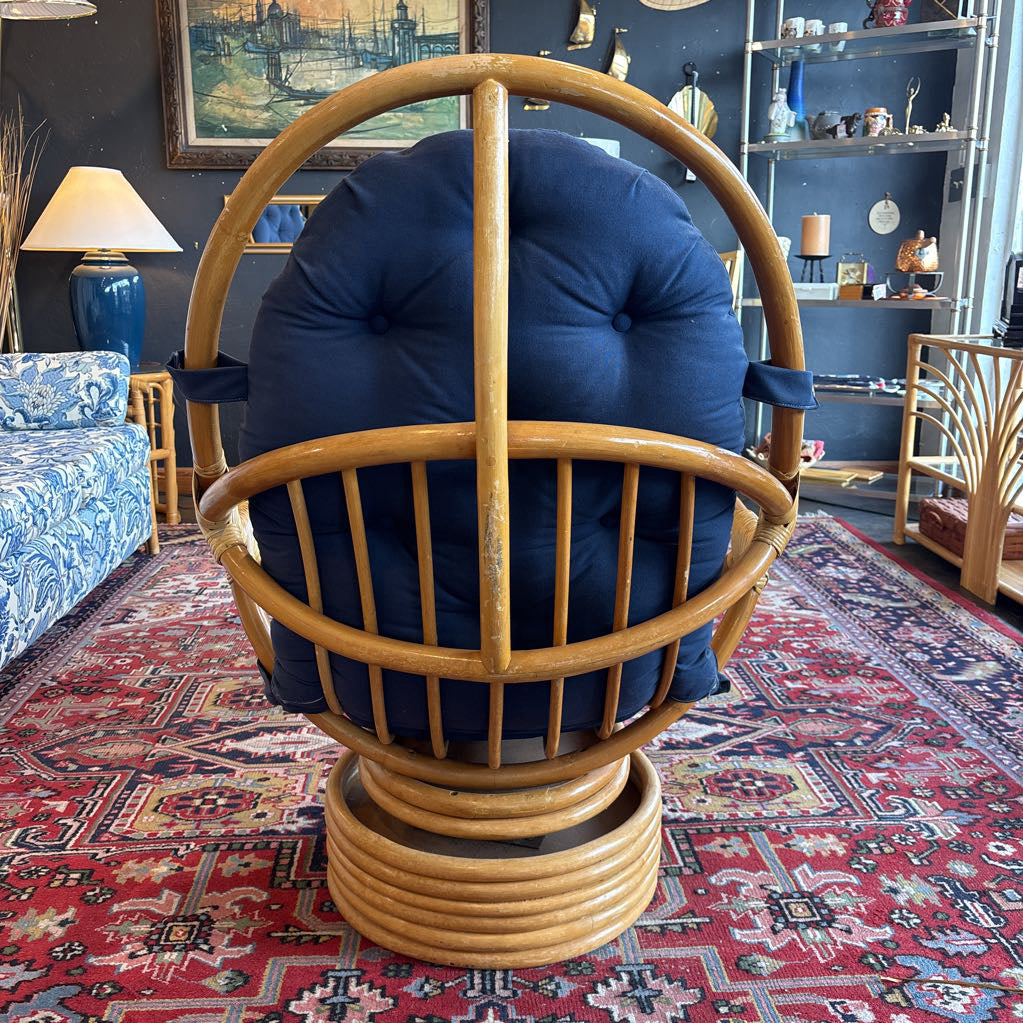 The back of a rattan and blue cushioned swivel chair in a room setting and on a red patterned rug.