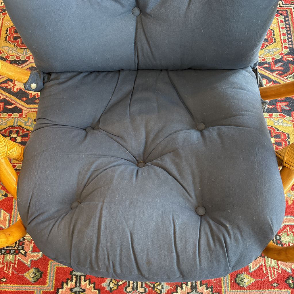 A blue cushion on a rattan frame and on a red patterned rug. 