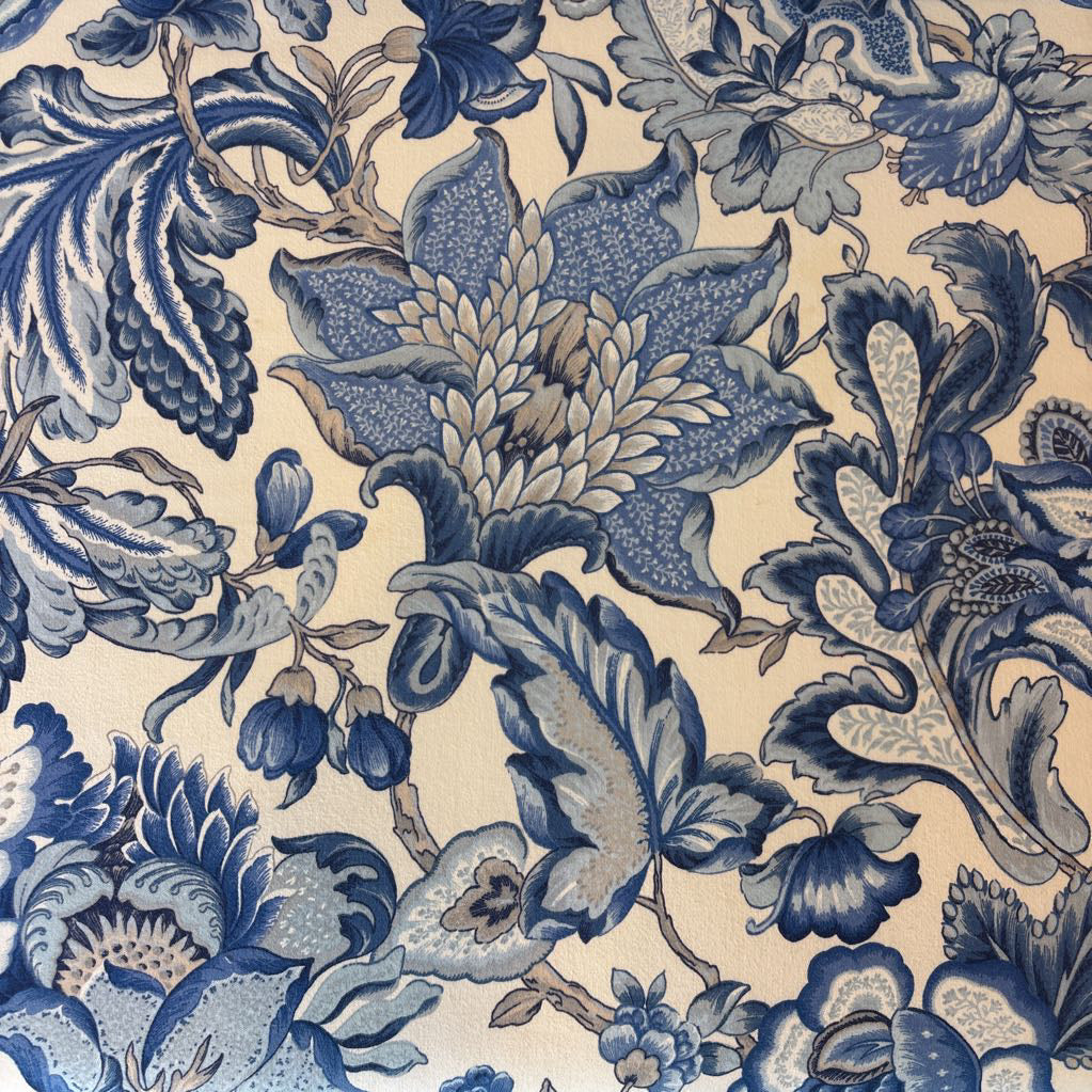 A close-up of a floral patterned fabric or wallpaper featuring blue and gray botanical motifs on a warm cream background.