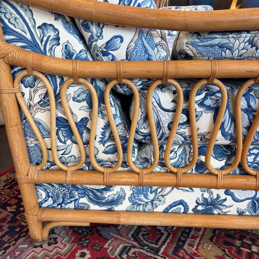 Close-up of a rattan or wicker sofa frame with blue and white floral patterned cushions, resting on a red patterned rug.