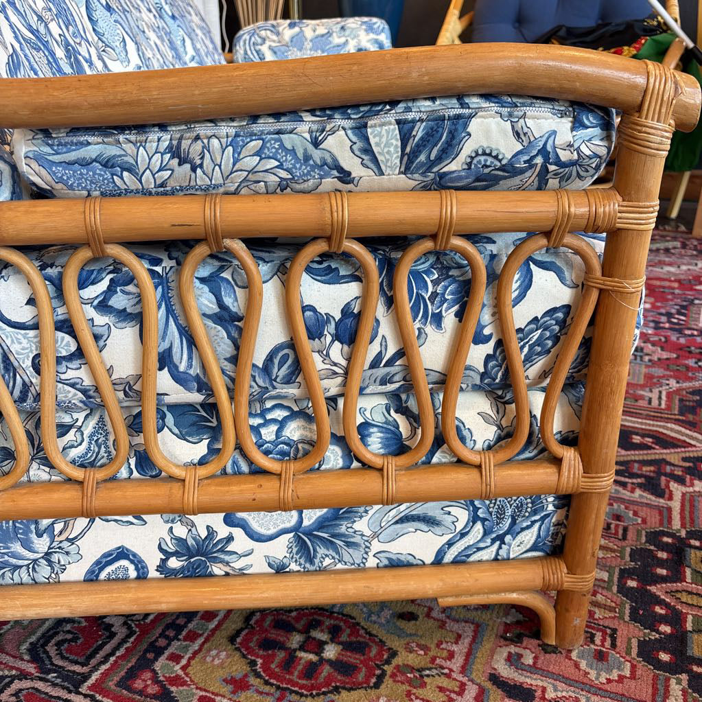 Close-up of a rattan or wicker sofa frame with blue and white floral patterned cushions, resting on a red patterned rug.