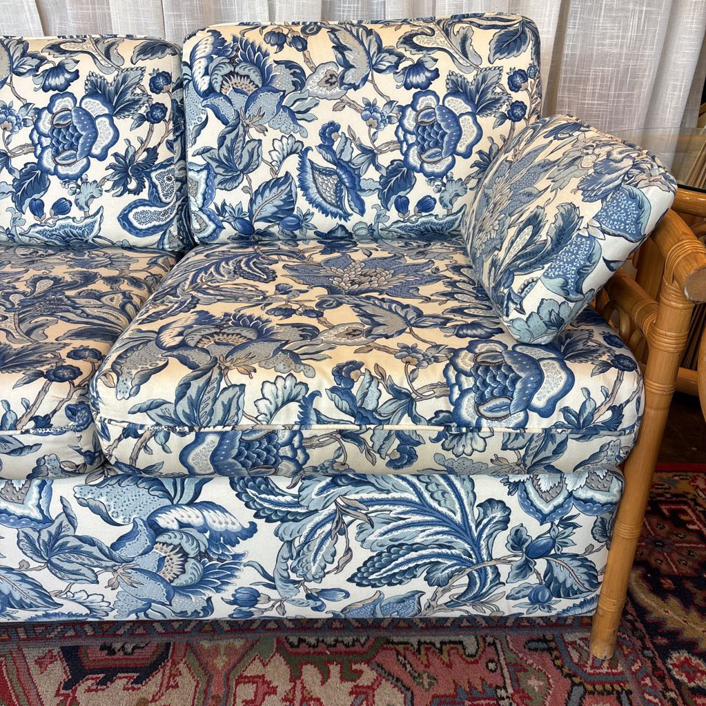 A close-up of a sofa upholstered in a blue and cream toile-style floral and bird pattern, with a wooden side table and patterned rug visible in the room setting.