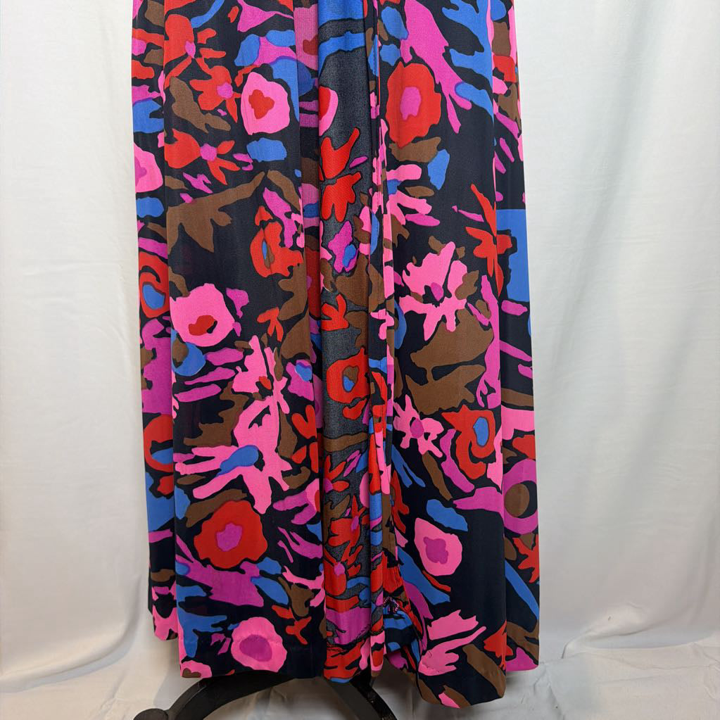 A long skirt with an abstract floral pattern in vibrant pink, red, blue, and brown on a black background, displayed on a stand against a white fabric backdrop.