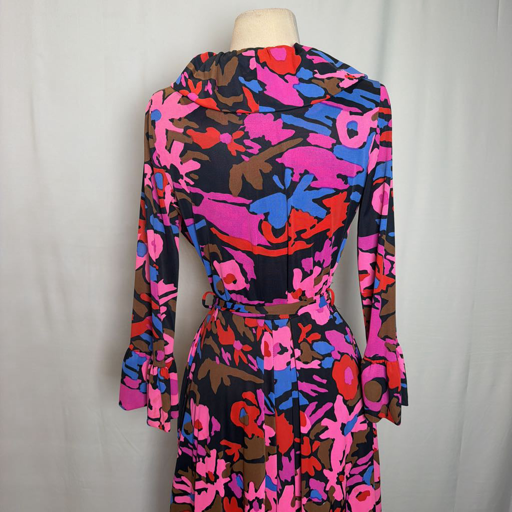 A long-sleeve belted wrap dress with a bold abstract floral print in pink, blue, red, and brown on a black background, displayed on a mannequin torso against a light gray fabric backdrop.