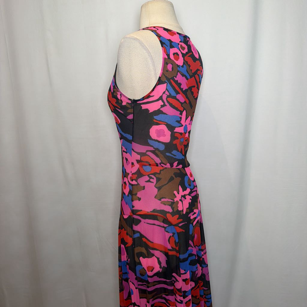 A sleeveless, scoop-neck maxi dress with a vibrant abstract floral pattern in pink, red, blue, and brown on a black background, displayed on a cream mannequin torso against a white fabric backdrop.