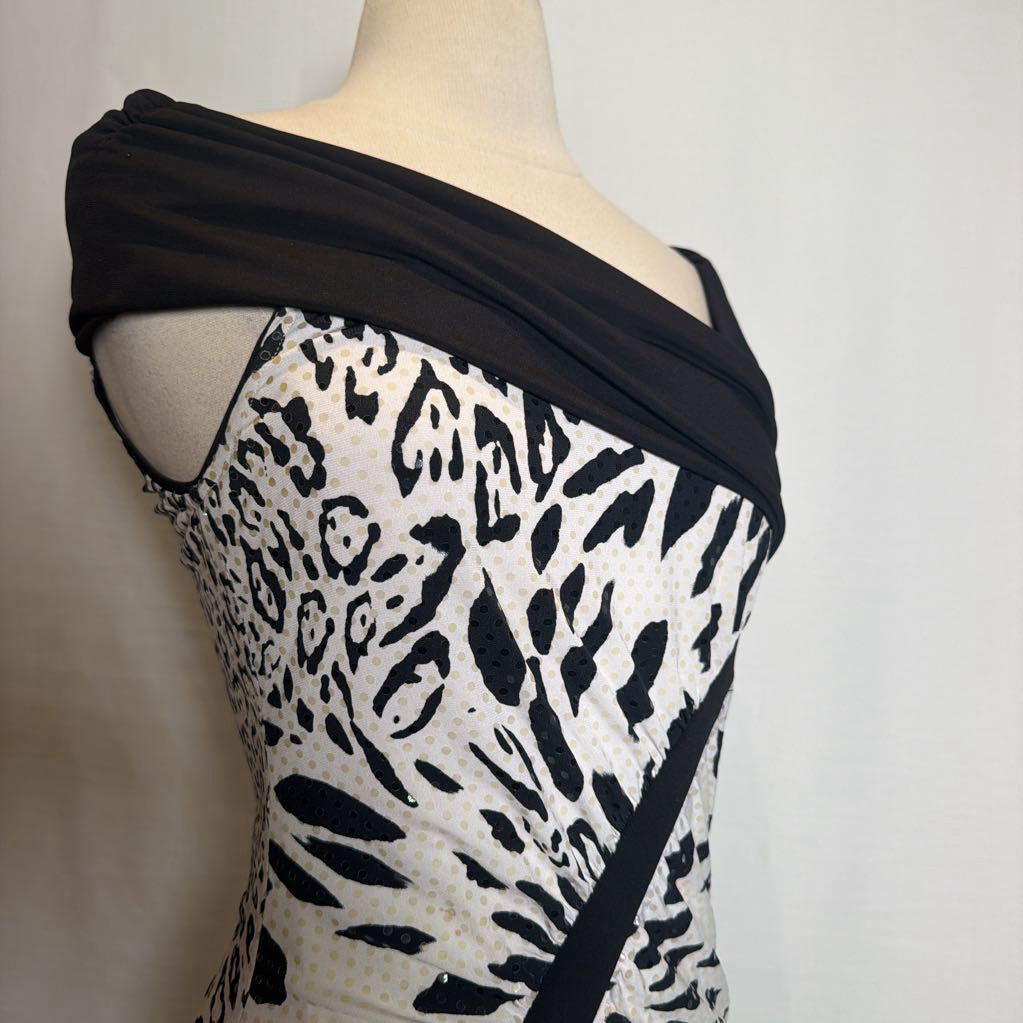 A black and white leopard print dress displayed on a beige mannequin torso, featuring a draped black fabric shoulder detail and a diagonal black sash.