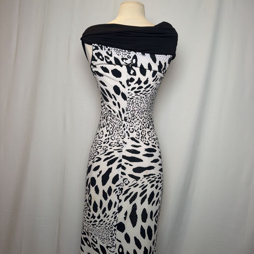 A black and white leopard print dress with a draped black neckline, displayed on a mannequin against a white curtain background.