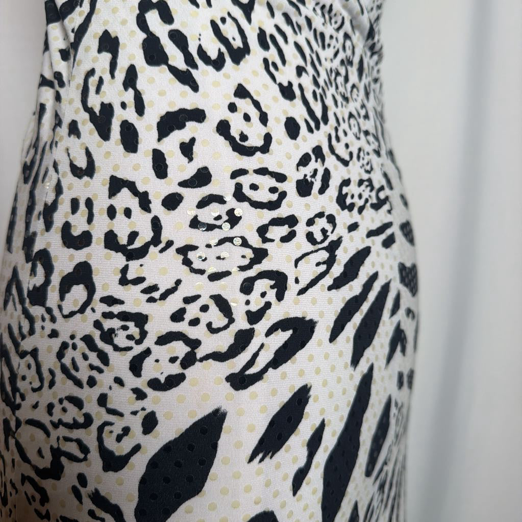 Close-up of a sleeveless dress with a black leopard print pattern on a warm off-white background with subtle gold polka dots.
