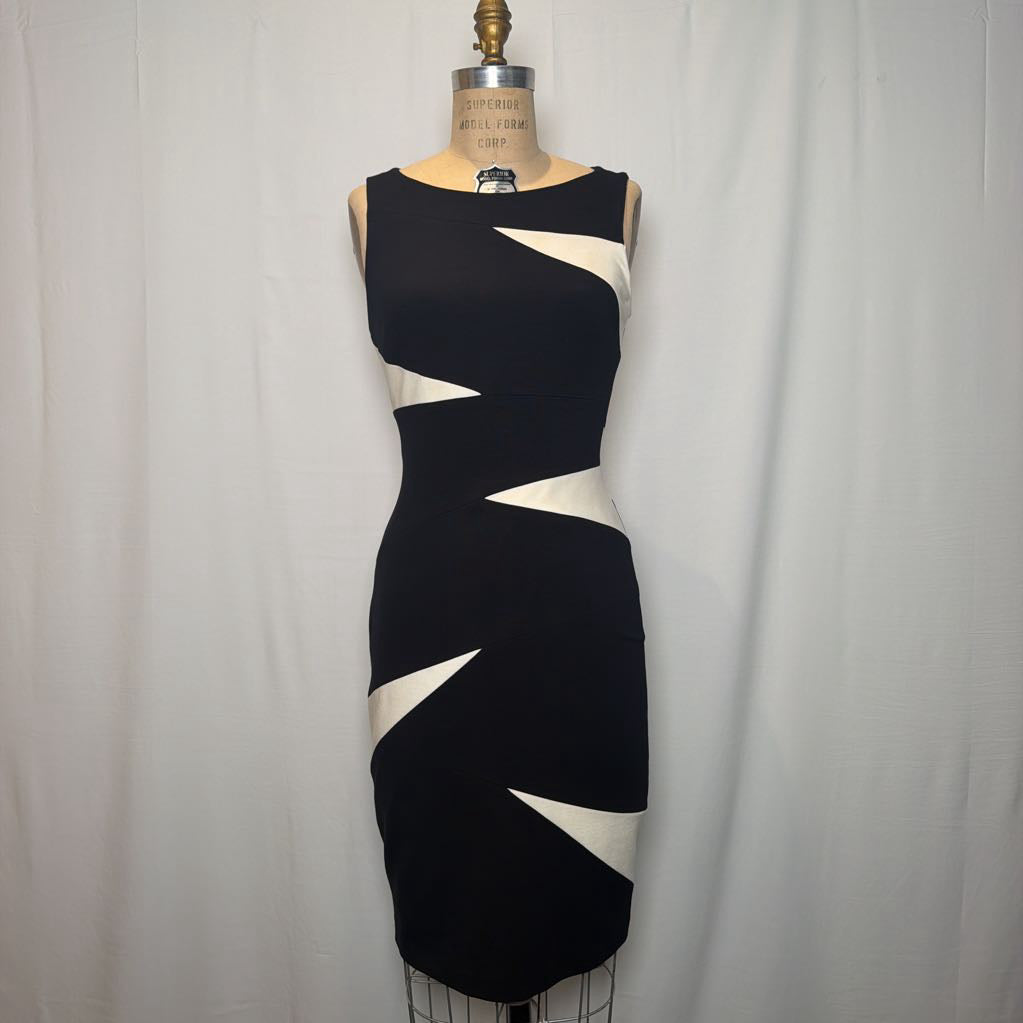 A sleeveless bodycon dress displayed on a dress form, featuring a black base with bold white geometric zigzag panels. The dress is photographed against a white fabric backdrop.