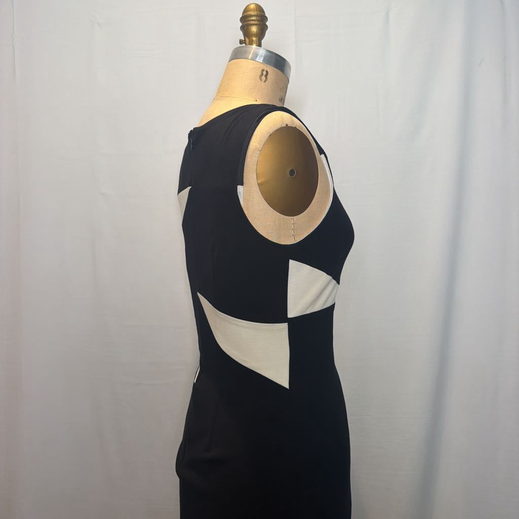 A sleeveless black dress with contrasting cream geometric panels, displayed on a wooden dress form mannequin against a white fabric backdrop.