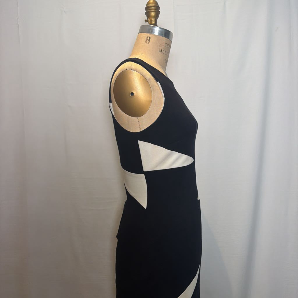 A sleeveless black dress with large white geometric color-block panels, displayed on a wooden dress form mannequin against a white fabric backdrop.