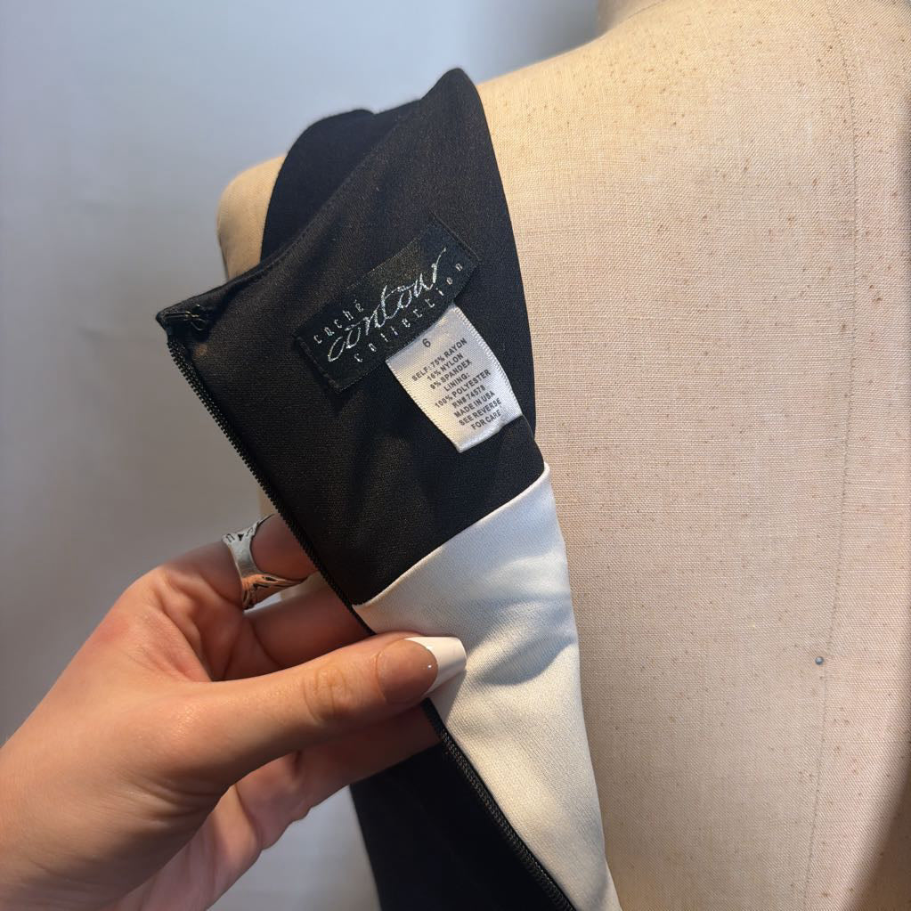 A close-up of a person's hand holding a black and white garment against a beige dress form. The garment has a black interior lining with a visible brand label reading 'FRESH Comfort Clothing' and a white size tag.