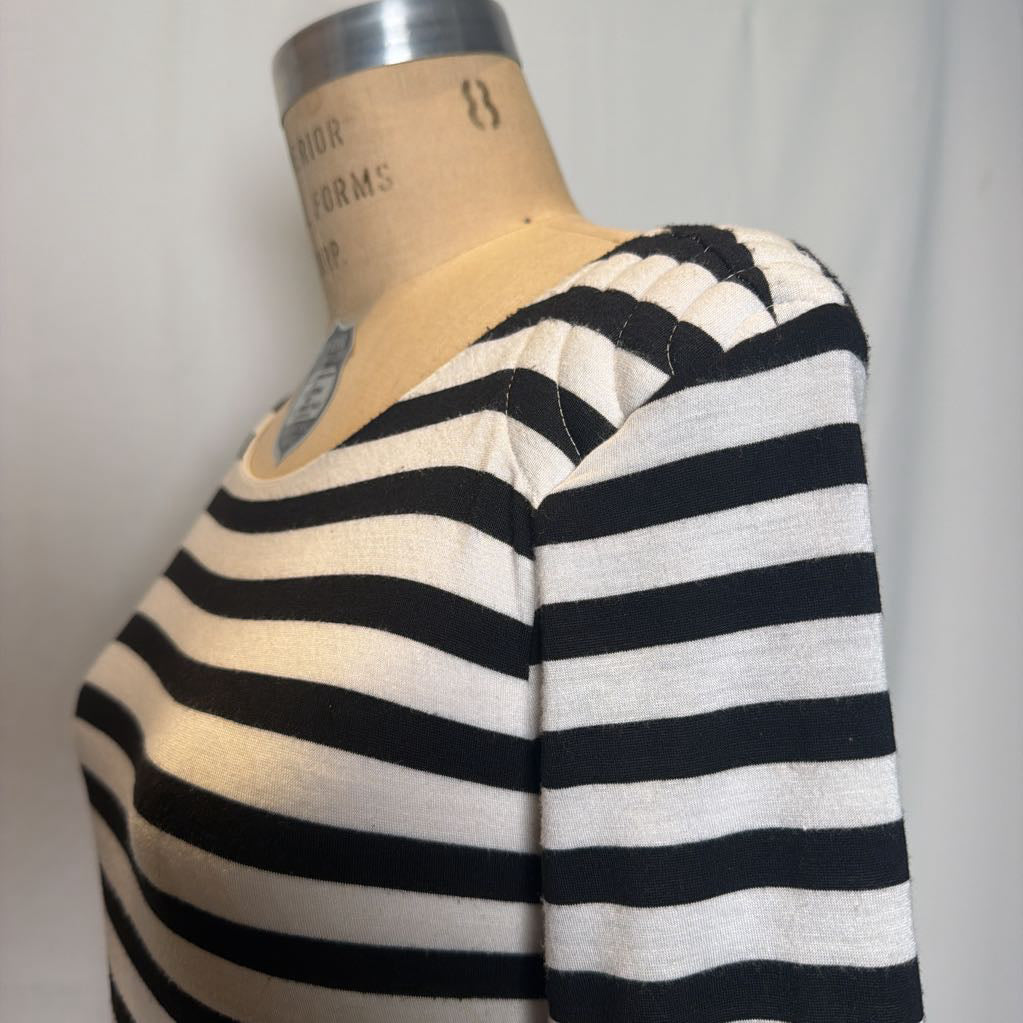 A close-up of a black and off-white horizontally striped knit top displayed on a dress form mannequin against a light gray background.