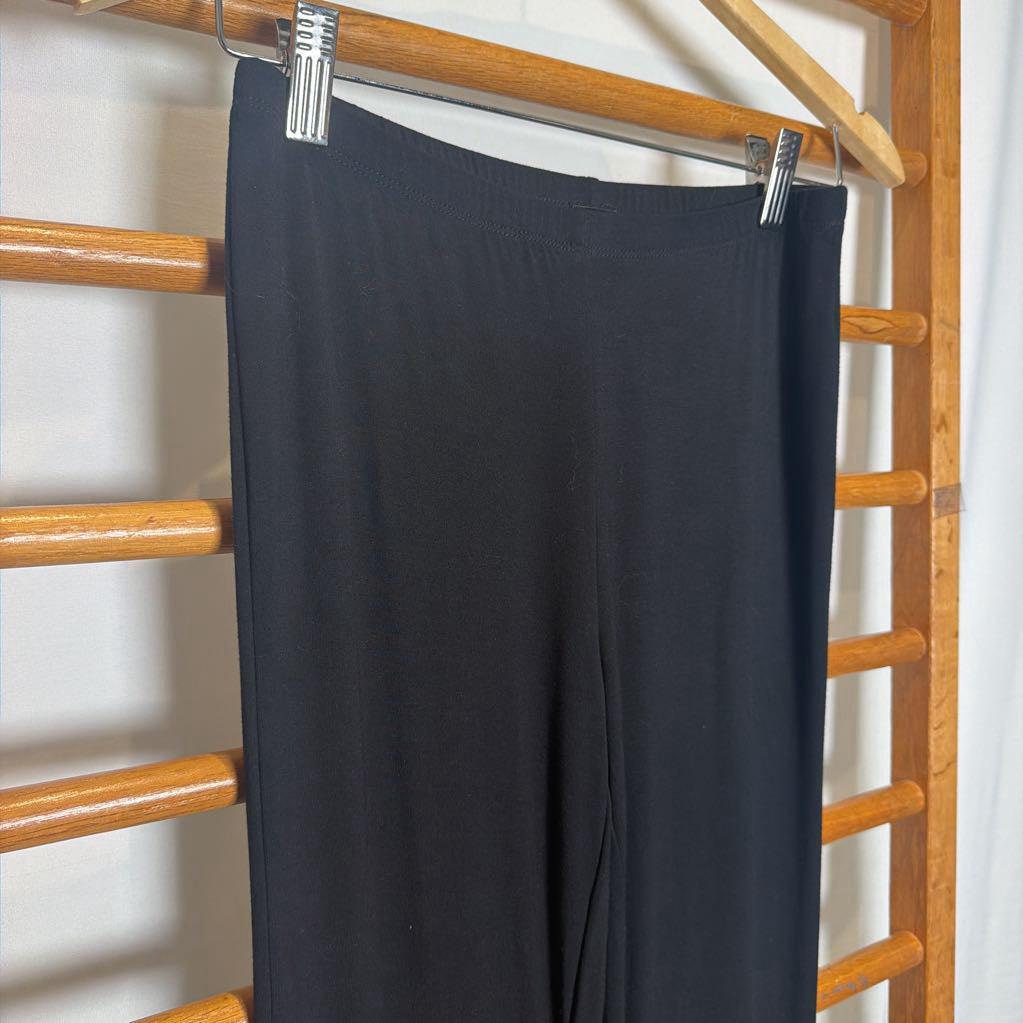 Black wide-leg pants hanging from a wooden hanger with metal clips on a wooden ladder rack.