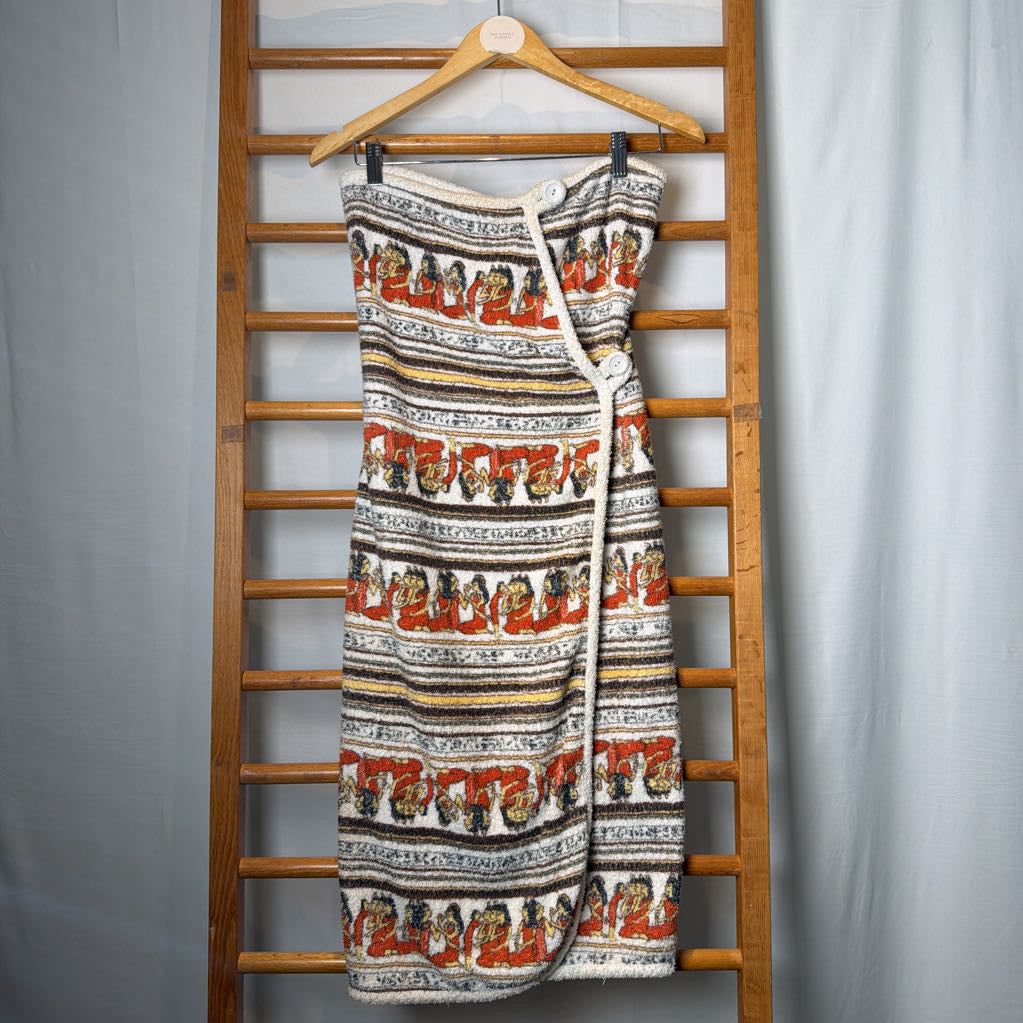 A sleeveless knit wrap dress with a colorful Southwestern-style pattern, hanging on a wooden hanger from a wooden ladder against a light gray backdrop.