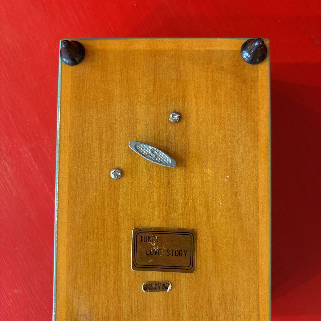 The bottom of wooden music box with a crank and a sticker that says 'TUNE: LOVE STORY' and 'Made in Taiwan Republic of China.'