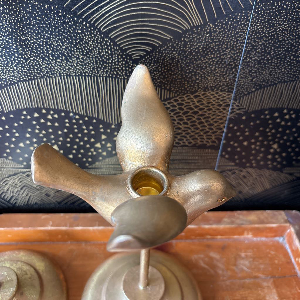 A brass oil lamp holder with a central cup containing oil, set against a patterned dark blue and black backdrop and a wooden surface below.