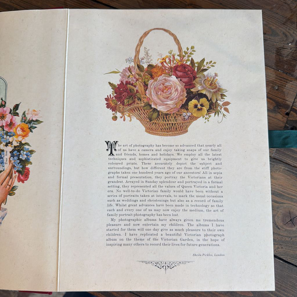 An open vintage-style printed book or album spread showing illustrated floral artwork with a basket and decorative text on aged cream paper, photographed on a dark wooden surface.