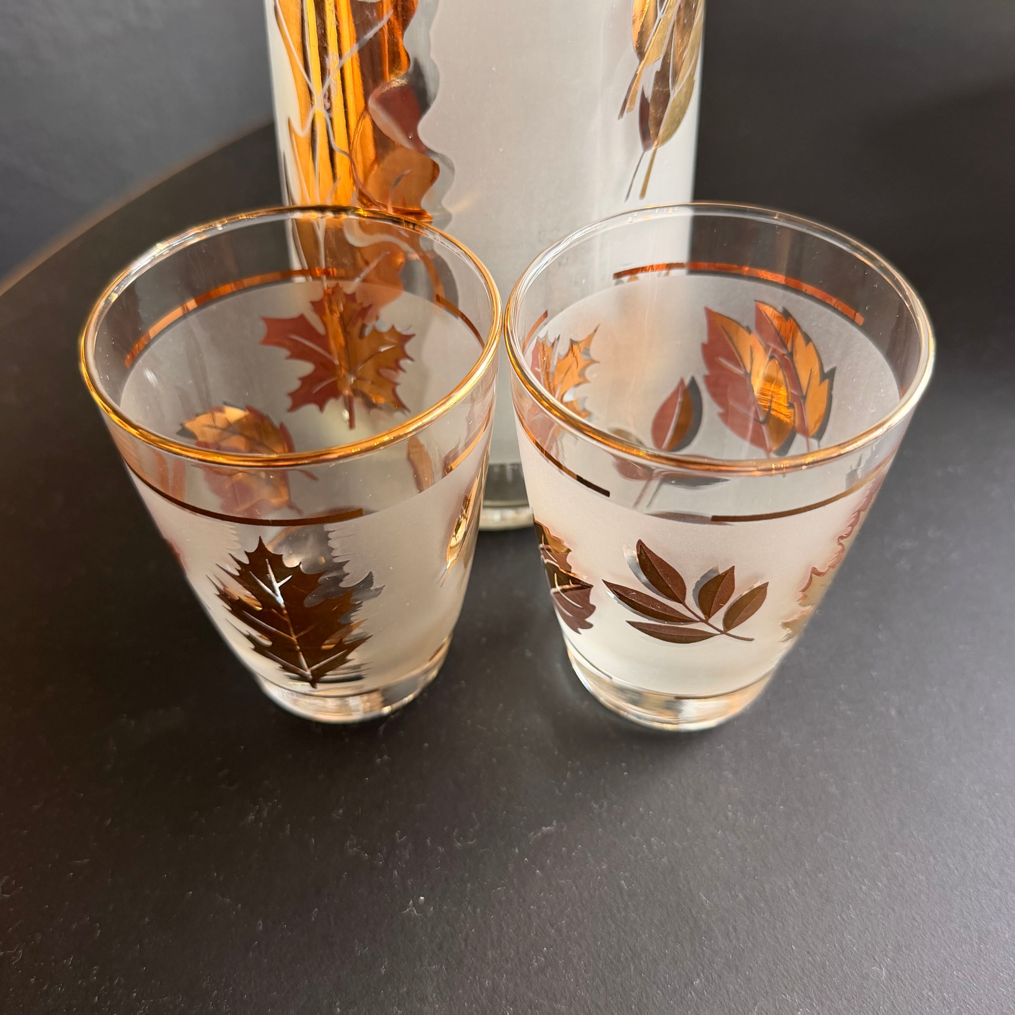 Two frosted clear shot glasses with gold and brown leaf patterns, shown alongside a matching tall glass on a dark surface.