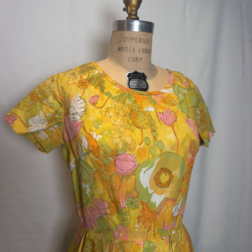 A vintage short-sleeve dress displayed on a wooden dress form. The dress features a vibrant yellow base with a retro floral pattern in pink, green, and orange.