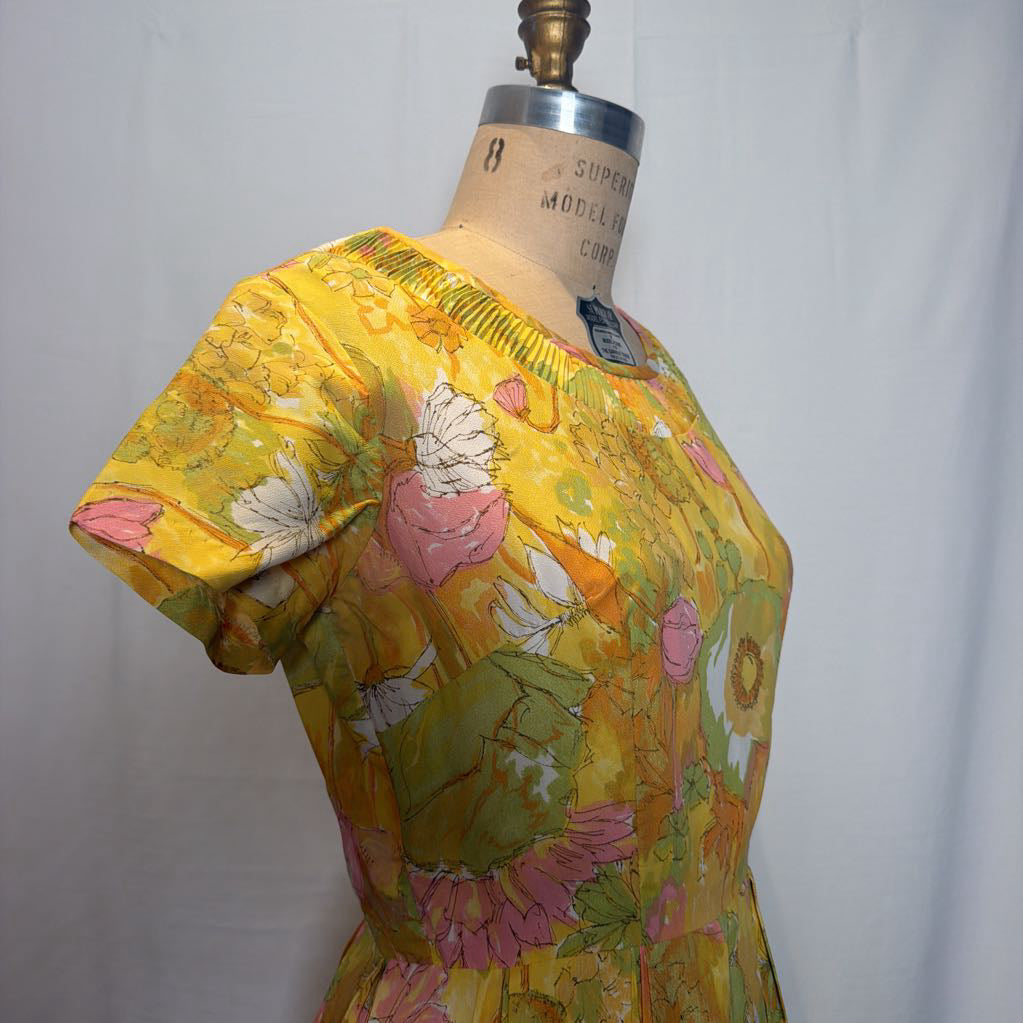 A vintage short-sleeve dress in a yellow floral print, displayed on a vintage wooden dress form mannequin against a white fabric backdrop.