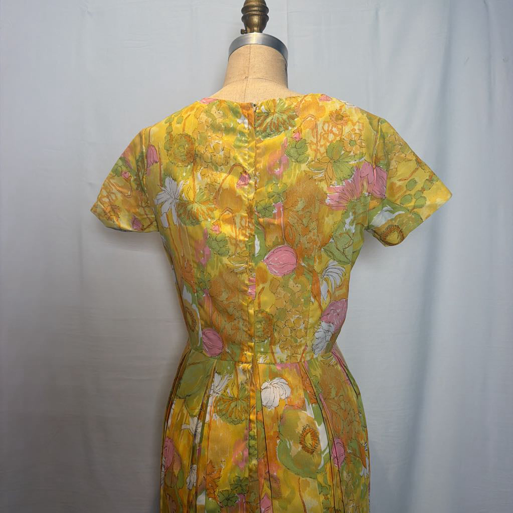 A vintage 1960s or 1970s floral print dress displayed on a dress form, showing the back view. The dress features a vibrant yellow base with pink, green, and orange floral patterns and a buttoned back.